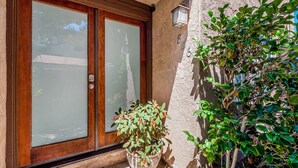 Une porte en bois avec des panneaux de verre dépoli, une plante en pot aux feuilles vertes et aux fleurs rouges, et une lanterne fixée au mur.