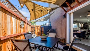 Une terrasse avec une table et des chaises, un barbecue et une vue sur l’intérieur de la maison.