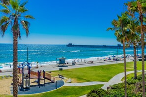 Une plage avec une aire de jeux, des palmiers et une jetée en arrière-plan.