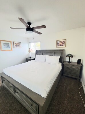 A bedroom with a bed, a nightstand, a lamp, a ceiling fan, and artwork on the walls.