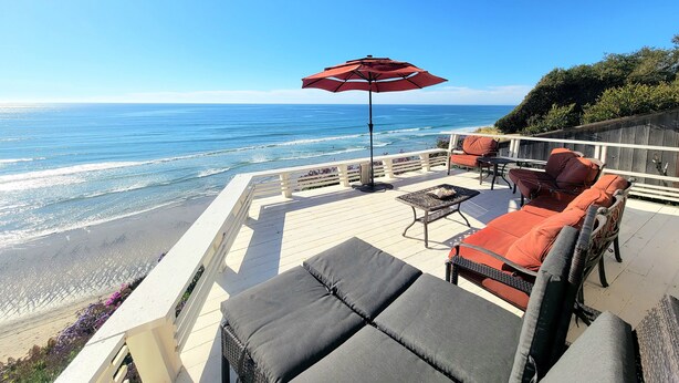 A deck with outdoor seating, a red umbrella, and a view of the ocean.