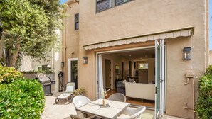 Un patio con mesa y sillas, una parrilla y vista hacia la casa.
