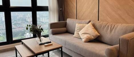 A modern living room with a sofa, a coffee table, and a view of a cityscape through large windows.