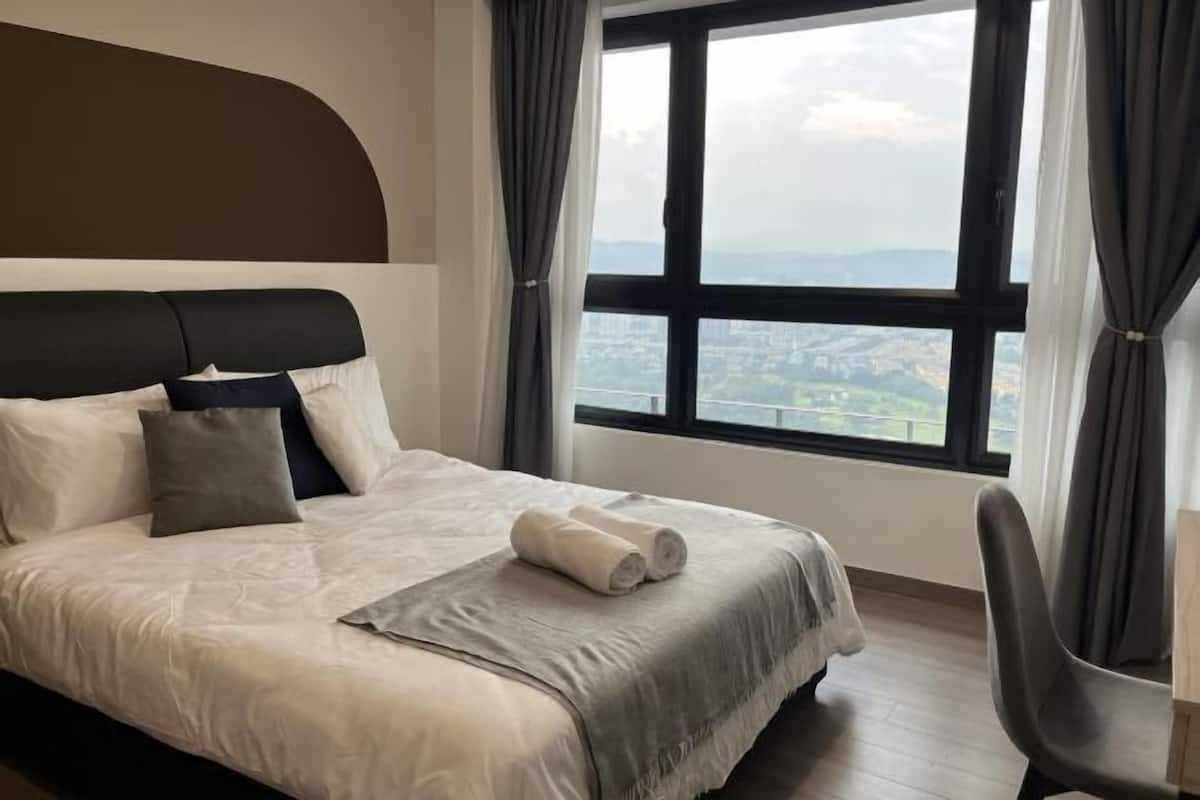 Ein Bett mit Kopfteil, Blick auf eine Stadtlandschaft durch ein großes Fenster und ein Sessel.
