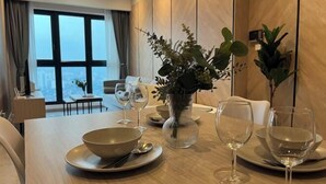 Ein Essbereich mit einem Tisch für zwei Personen, einer Pflanzvase und Blick auf die Stadt durch große Fenster.