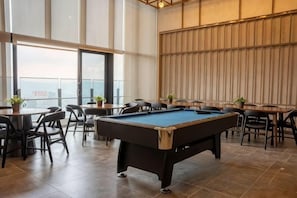 Een biljarttafel in een ruimte met stoelen en tafels, grote ramen en een uitzicht.