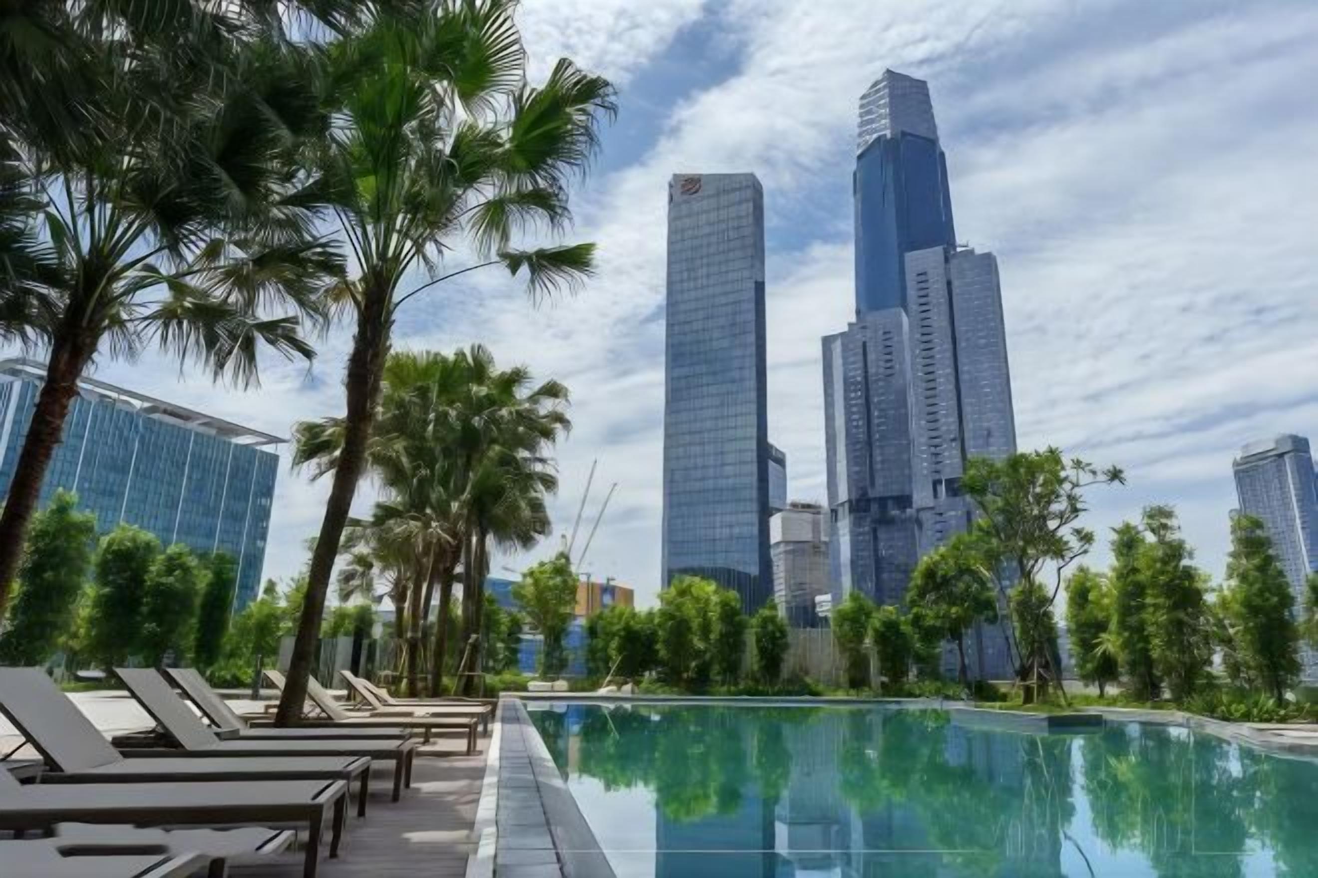 A poolside area with lounge chairs, palm trees, and a city skyline in the background.