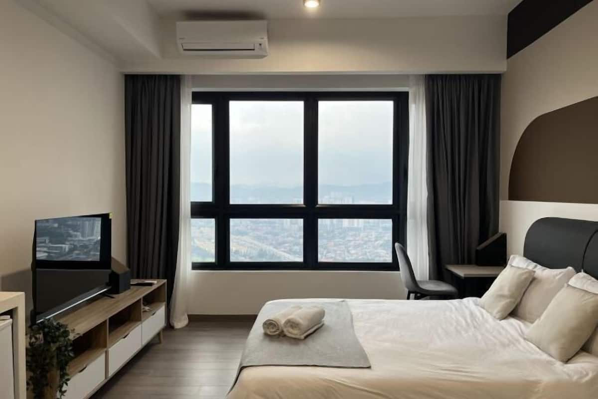 Ein Hotelzimmer mit Bett, Fernseher, Schreibtisch und großem Fenster mit Blick auf die Stadt.