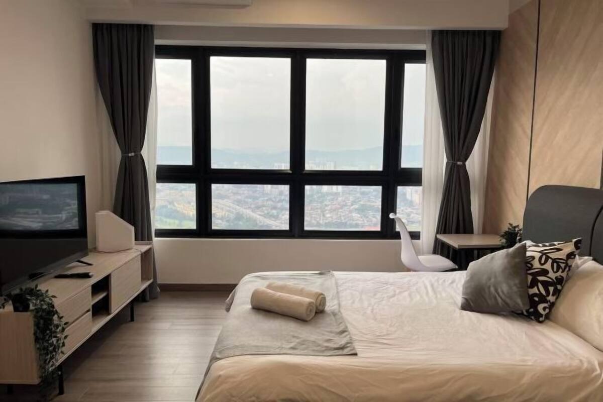 Ein Hotelzimmer mit großem Fenster, einem Bett, einem Fernseher, einem Schreibtisch und einem Sessel.