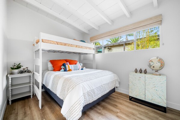 A bedroom with a bunk bed, a white bedside table with a plant, a globe, and a patterned cabinet. - Tropical Island Oasis Home (Encinitas)