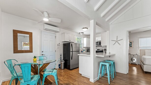 A modern kitchen with white cabinetry, a stainless steel refrigerator, and a dining area with turquoise chairs and a glass table.