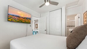 A bedroom with a bed, a ceiling fan, a TV displaying a sunset, and white doors.
