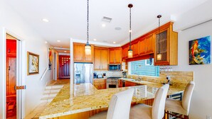 A modern kitchen with wooden cabinets, granite countertops, and bar seating. - Luxury Beachfront Getaway - Main House (Oceanside)