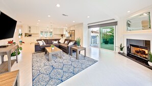A spacious living area with a fireplace, a large sofa, and a kitchen in the background. - Enchanting Cottage by the Sea (Carlsbad)