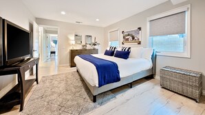 A modern bedroom with a large bed, a television, and a wicker storage unit. - Enchanting Cottage by the Sea (Carlsbad)