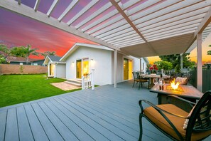 Eine überdachte Terrasse mit Tisch und Stühlen, ein kleines Haus mit einer Tür und ein Rasengrundstück.