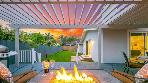 A patio with a fire feature, outdoor seating, and a view of a backyard. - Enchanting Cottage by the Sea (Carlsbad)