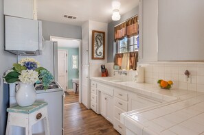 A kitchen with white cabinets, a sink, a vase with flowers, and a fruit bowl.