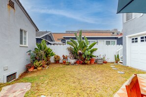 A backyard with a white fence, various potted plants, a stone pathway, and a wooden bench.