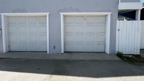A building with two garage doors and a white picket fence. - The Strand Cottage Beachfront (Oceanside)