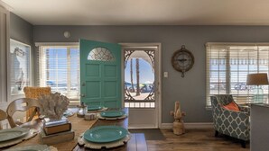 A dining area with a teal door, a view of the beach, and a patterned armchair.