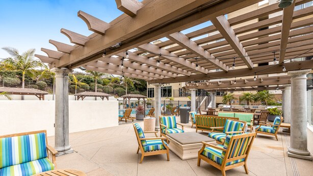 Un espace extérieur aménagé en terrasse, avec des meubles en bois, une pergola et une piscine en arrière-plan.