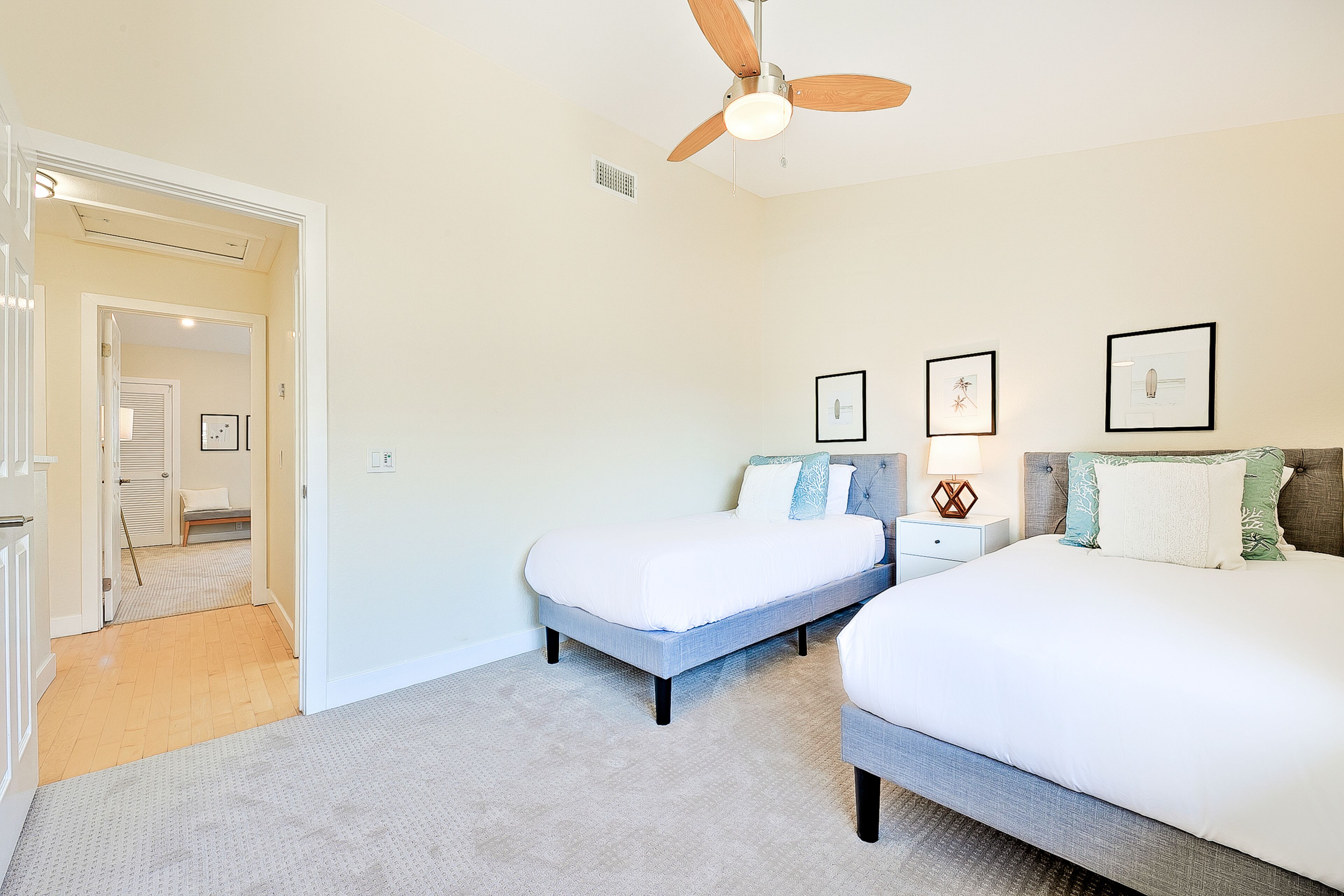 A bedroom with two beds, a ceiling fan, and framed pictures on the wall.