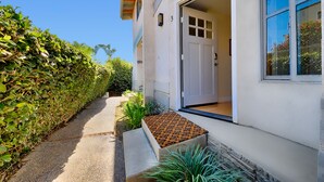 Ein Wohngebäude mit weißer Fassade, einer Garagentür und einem kleinen Garten mit Pflanzen und einem Betonpflanzkübel.