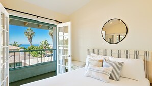 Ein Schlafzimmer mit einem großen Bett, einem runden Spiegel und Blick auf das Meer durch eine geöffnete Tür.
