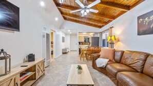 Uma sala de estar com teto de madeira, um ventilador de teto, um sofá de couro marrom, uma mesa de centro de madeira e uma TV na parede.