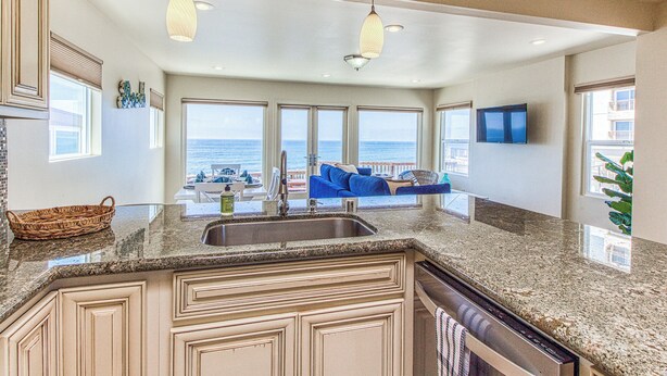 A kitchen with granite countertops, a built-in sink, and a view of the ocean through large windows. - Ocean Beach Cliffs Sanctuary Oceanfront (San Diego)