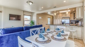A modern kitchen with white cabinets, a dining area with a white table set for four, and a blue sofa in the living area. - Ocean Beach Cliffs Sanctuary Oceanfront (San Diego)
