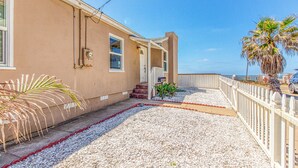 A beachfront house with a covered porch, a small front yard with gravel and plants, and a white fence. - Ocean Beach Cliffs Sanctuary Oceanfront (San Diego)