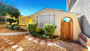 A residential house with a yellow facade, a wooden gate, and a paved driveway with stepping stones.