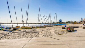 Una playa con barcos alineados en la arena, cielo despejado y edificios al fondo.