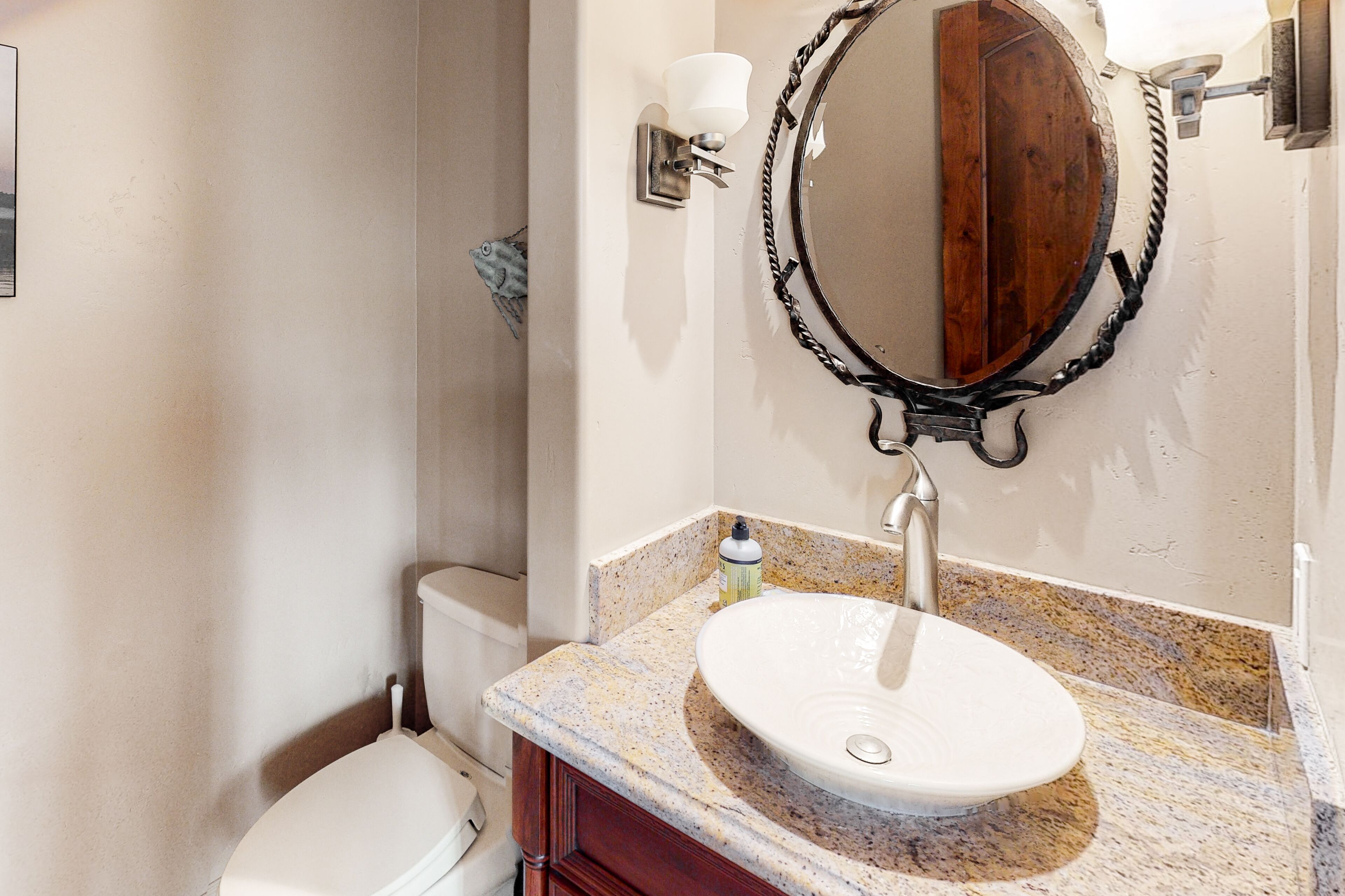 A bathroom with a white toilet, a sink with a marble countertop, and a wooden-framed mirror.