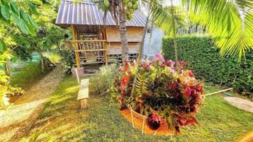 Una estructura de madera con balcón, rodeada de exuberante follaje y un arreglo de flores colgantes.