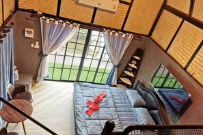 A room with a bed, a chair, a small table, and a view of a green outdoor area through large windows. - khao Thung Benja HomeStay (Phayuha Khiri)