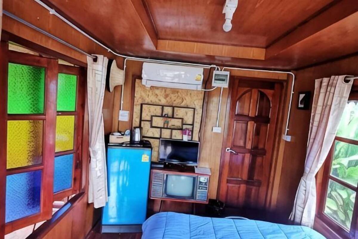 Una habitación pequeña con cama, televisión, refrigerador y un mueble de madera.
