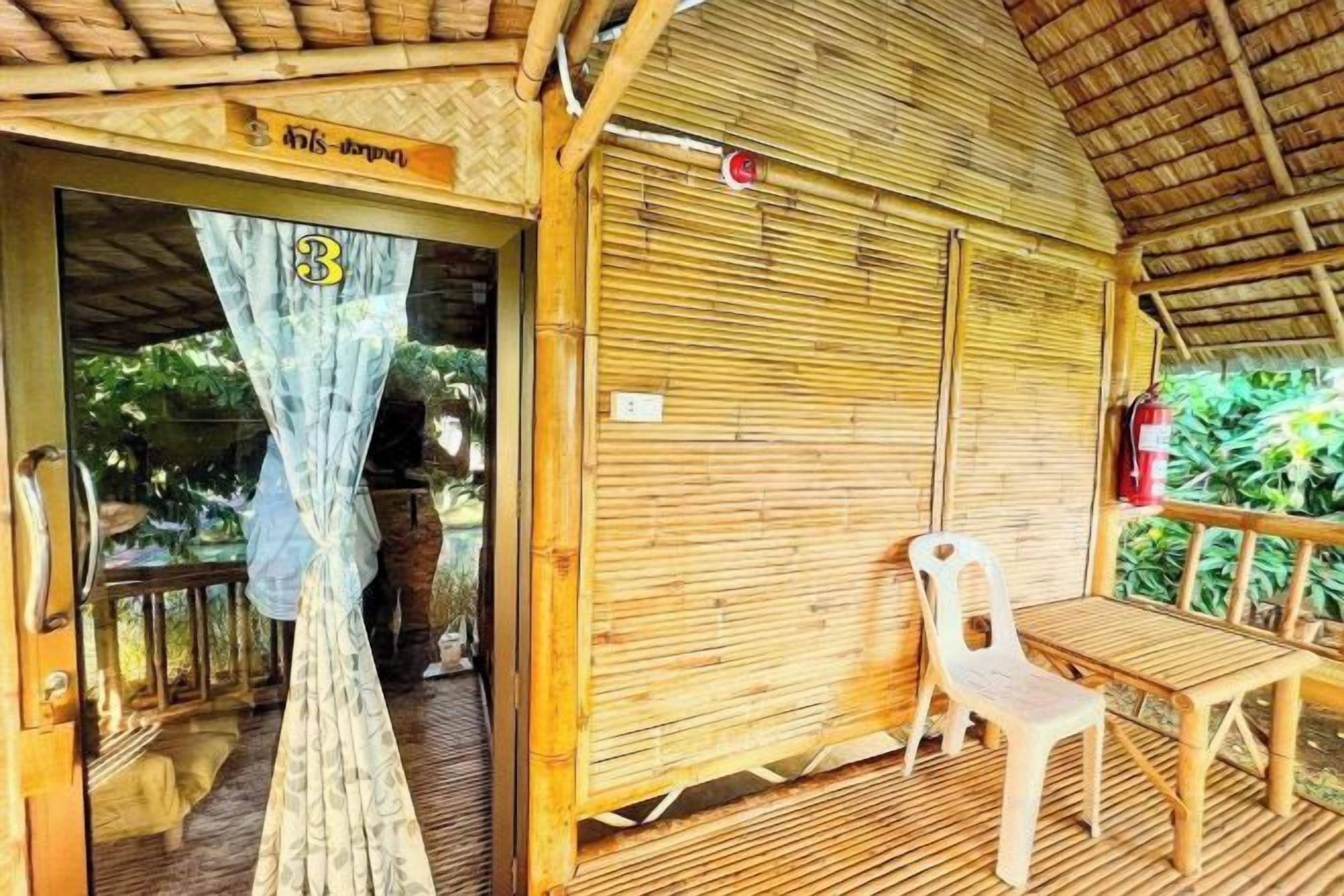 A room with a bamboo ceiling, a closed door, a window with a curtain, and a table with a chair.