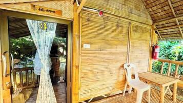 A room with a bamboo ceiling, a closed door, a window with a curtain, and a table with a chair.