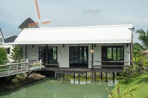 A white building with a dock extending into a body of water, surrounded by greenery. - khao Thung Benja HomeStay (Phayuha Khiri)