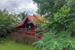 A wooden house with a red roof, surrounded by lush greenery and trees. - khao Thung Benja HomeStay (Phayuha Khiri)