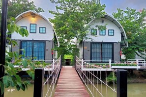 A wooden bridge leading to a row of white buildings with large windows, surrounded by greenery. - khao Thung Benja HomeStay (Phayuha Khiri)