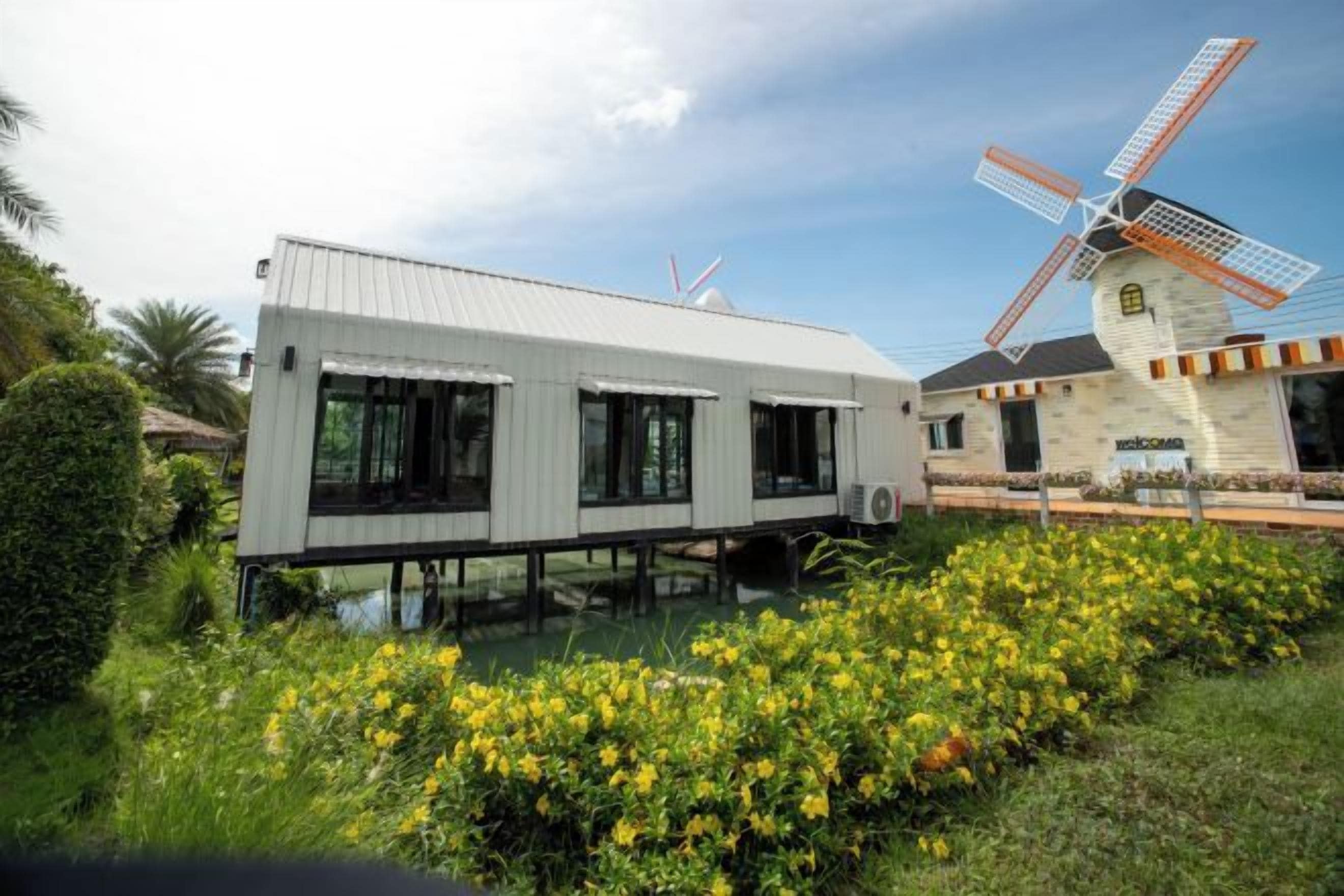 Een modern gebouw met een windmolen op de achtergrond, een waterpartij in de voorgrond en een bord waarop staat 'Welcome'.