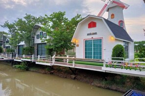 Un bâtiment blanc surmonté d’un moulin à vent rouge, avec une grande porte de garage et un petit porche doté d’une balustrade.