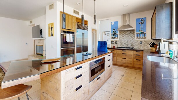Una cocina moderna con una isla grande, electrodomésticos de acero inoxidable, armarios de madera e iluminación colgante.