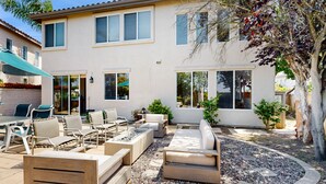 Una casa moderna con un patio que cuenta con mobiliario exterior, una mesa de comedor y un hogar.