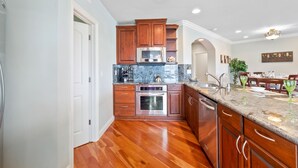 A modern kitchen with wooden cabinets, stainless steel appliances, and a marble countertop. - Buccaneer Beach Lookout - 30-Night Minimum (Oceanside)