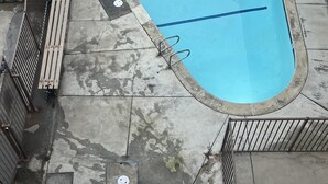 An outdoor swimming pool with a small adjacent hot tub, surrounded by a concrete deck and metal fencing. - Blue Wave Penthouse Oceanview (San Diego)